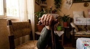 Elderly man's hands holding wooden cane in natural light, representing living with Parkinson's disease and neurological conditions