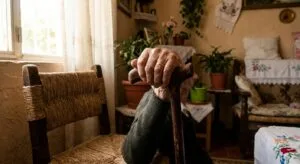 Elderly man's hands holding wooden cane in natural light, representing living with Parkinson's disease and neurological conditions
