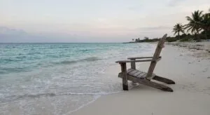 Empty wooden chair facing calm turquoise waters on a quiet Cozumel beach at dawn, symbolizing contemplation and new possibilities in depression treatment