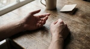 Two hands resting on a wooden table in natural light, conveying contemplation and vulnerability in considering mental health treatment options